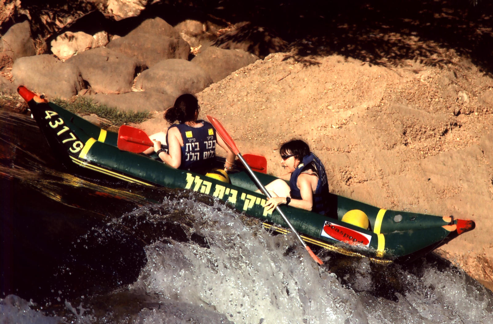 A vintage photo of two people white water rafting backwards over a waterfall