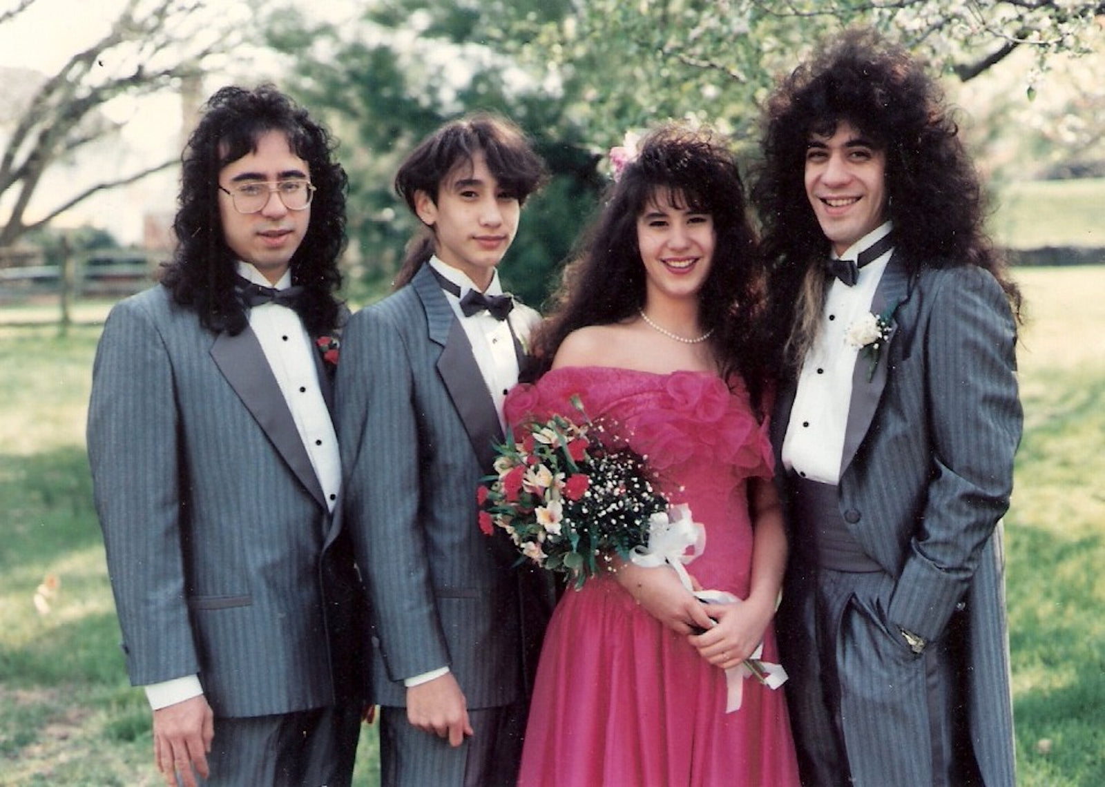 A vintage family photo of three men and a woman with very large permed 80s hairdos