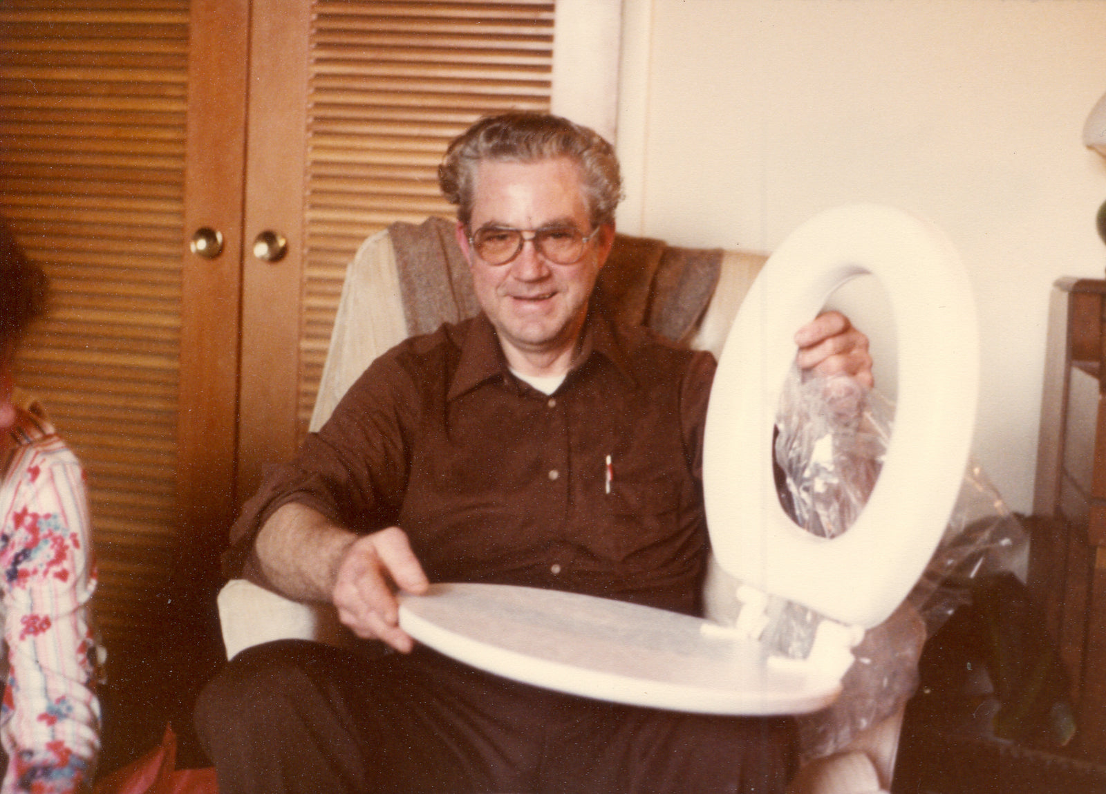 Vintage photo of a middle aged man holding up a toilet seat he had just unwrapped. 