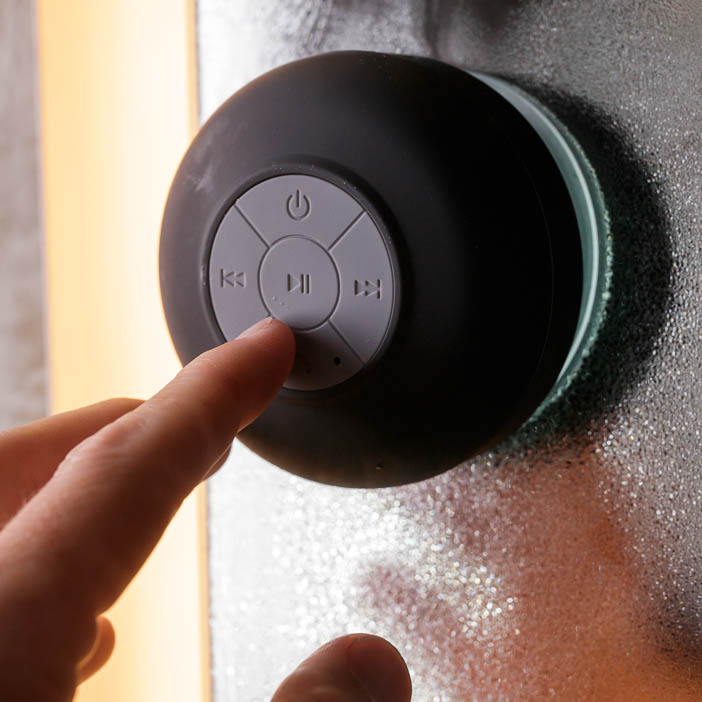 A man pressing play on a waterproof shower bluetooth speaker